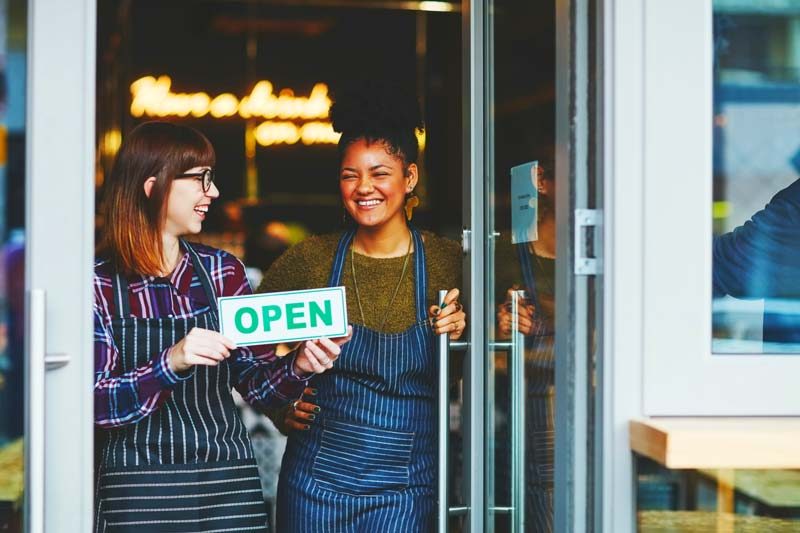 Two small business women turning the open sign